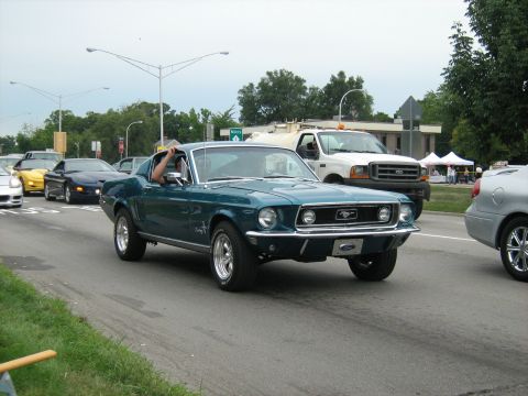 1988 Mercury Grand Marquis - Classic teal Ford Mustang coupe in motion during a car event, with other vehicles in the background.