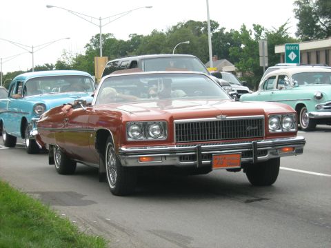 1988 Mercury Grand Marquis - This orange convertible, likely a 1975 model, is seen in traffic with other classic cars.