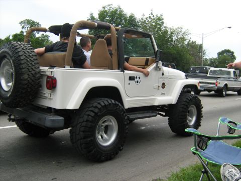 1988 Mercury Grand Marquis - A white Jeep Wrangler with a spare tire on the back is driving down a road with other vehicles.