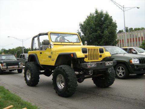 1988 Mercury Grand Marquis - A yellow Jeep Wrangler drives down a street alongside other vehicles.