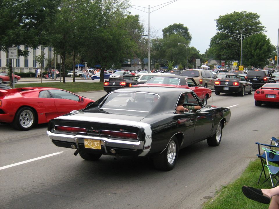 Black 1970 Dodge Charger driving in traffic, red Lamborghini in front