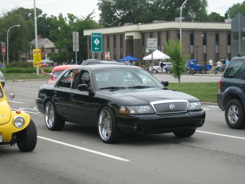 1988 Mercury Grand Marquis - A black sedan drives down the road with custom chrome wheels.