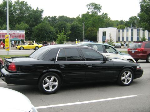 1988 Mercury Grand Marquis - A black sedan is parked on the street, with other vehicles and buildings in the background.