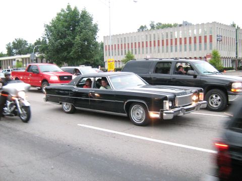 1988 Mercury Grand Marquis - A black 1977 Lincoln Continental Mark IV cruises down the road, part of a larger scene with other vehicles.