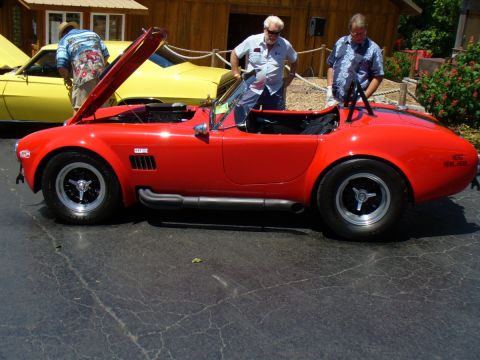 1995 Ford Thunderbird - A red convertible sports car is displayed at an outdoor car show with people around.