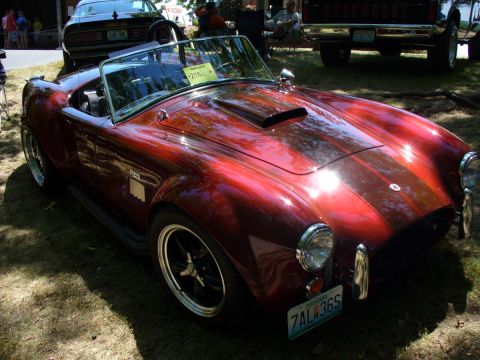 1995 Ford Thunderbird - A shiny red convertible sports car with racing stripes is parked on grass at a car show.