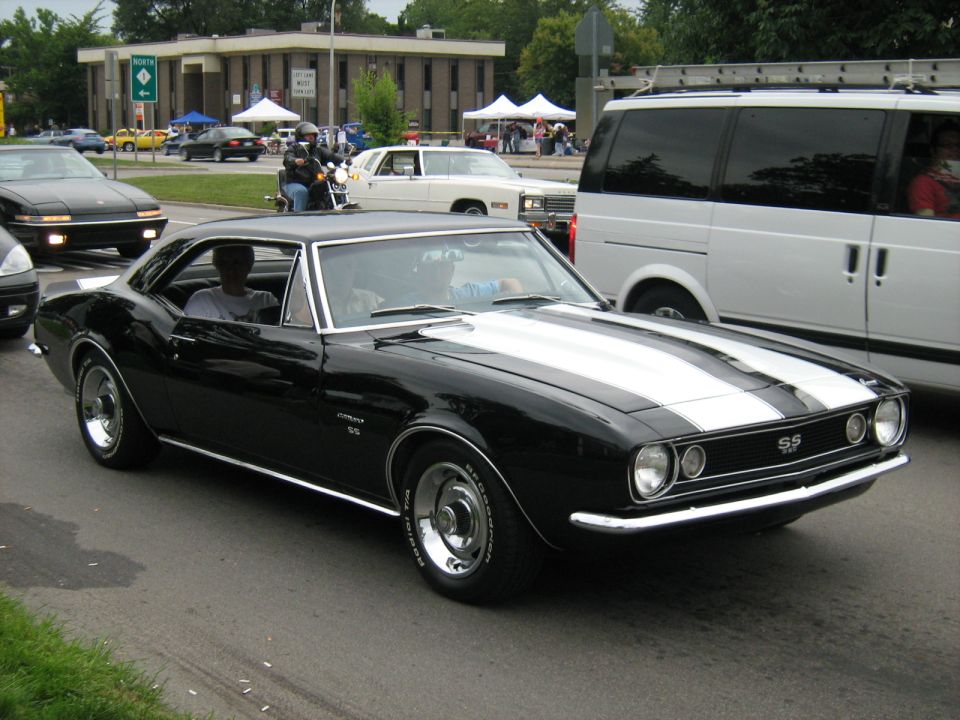 Black 1967 Chevrolet Camaro SS with white racing stripes, chrome wheels, and a driver
