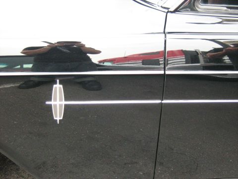 1988 Mercury Grand Marquis - A Lincoln emblem is visible on the side of a black car, with reflections of other vehicles in the paint.