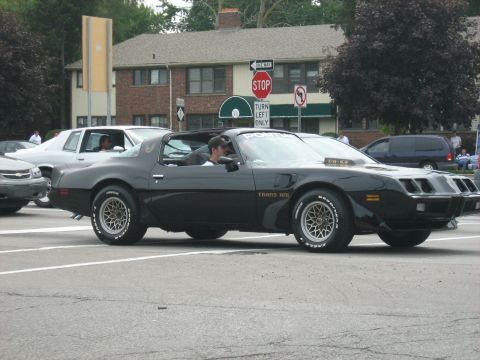 1988 Mercury Grand Marquis - Black 1977 Pontiac Trans Am with gold trim and honeycomb wheels driving on a street.
