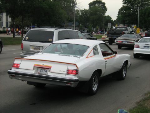 1988 Mercury Grand Marquis - A white coupe with distinctive orange and yellow stripes on its rear is seen on the road.