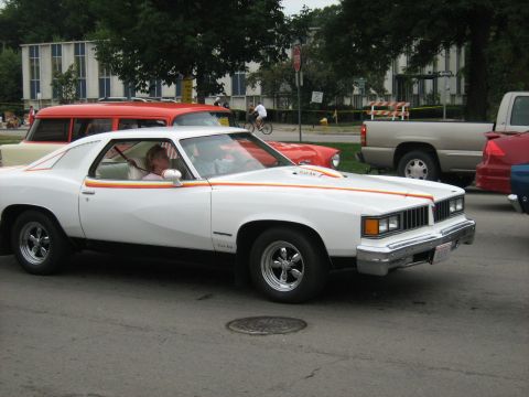 1988 Mercury Grand Marquis - White 1975 Pontiac Grand Am coupe with distinctive side stripes and chrome wheels parked on a street.