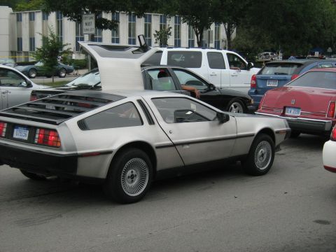 1988 Mercury Grand Marquis - A DeLorean DMC-12 is parked in a lot, its distinctive gullwing doors are raised.