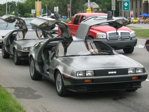 1988 Mercury Grand Marquis - Multiple DeLorean DMC-12s with gullwing doors open are seen on the road.