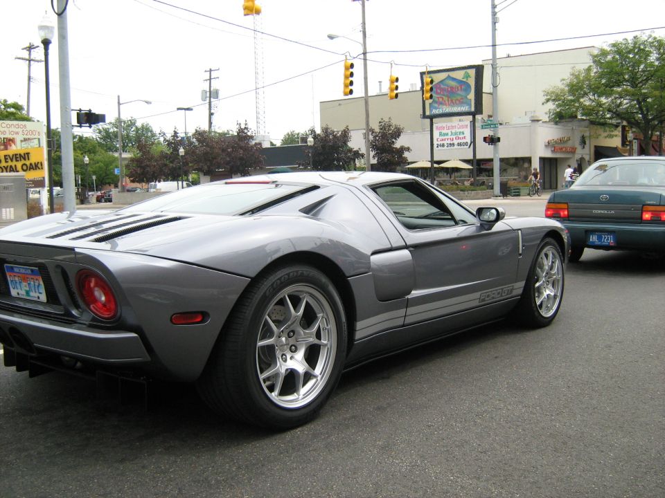 Gray Ford GT with racing stripes on the side, driving on a street. Another car is visible behind it