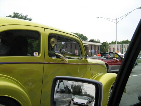 1988 Mercury Grand Marquis - An alien figure appears to be driving a vintage lime green car in traffic.