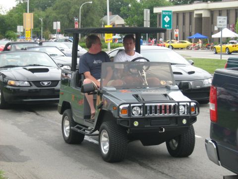 1988 Mercury Grand Marquis - A golf cart designed to look like a Hummer H2 is driven by two men during a car show.