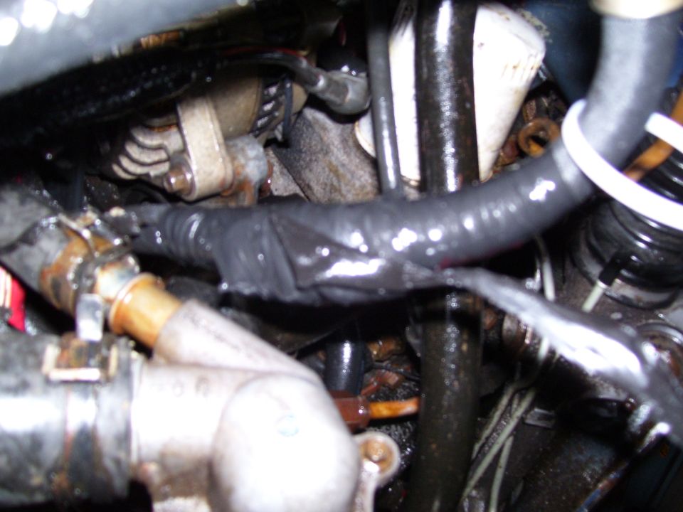 Close-up of engine bay hoses, taped wiring harness, and corroded metal coolant housing