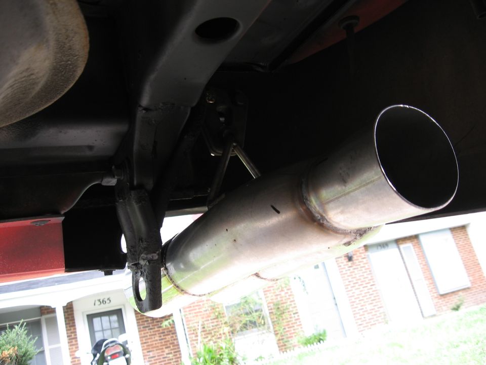 close-up of a car's exhaust pipe and undercarriage, with a house in the background