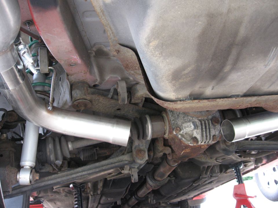Undercarriage view of a car showing the differential, exhaust pipes, suspension components, and fuel tank