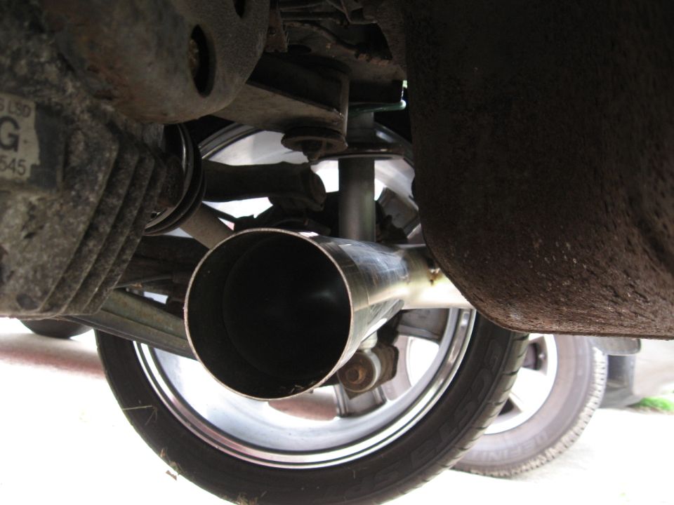 Close-up of a car's exhaust pipe and part of the rear suspension system, with a wheel visible