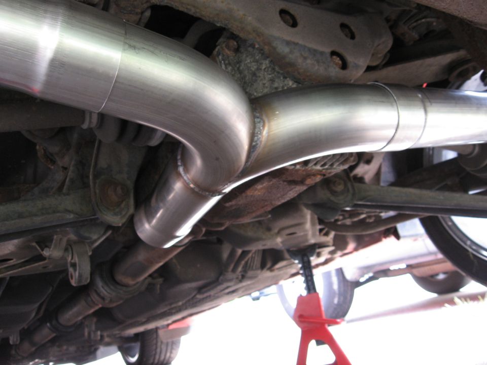 Custom exhaust pipes installed under a vehicle, supported by a red jack stand