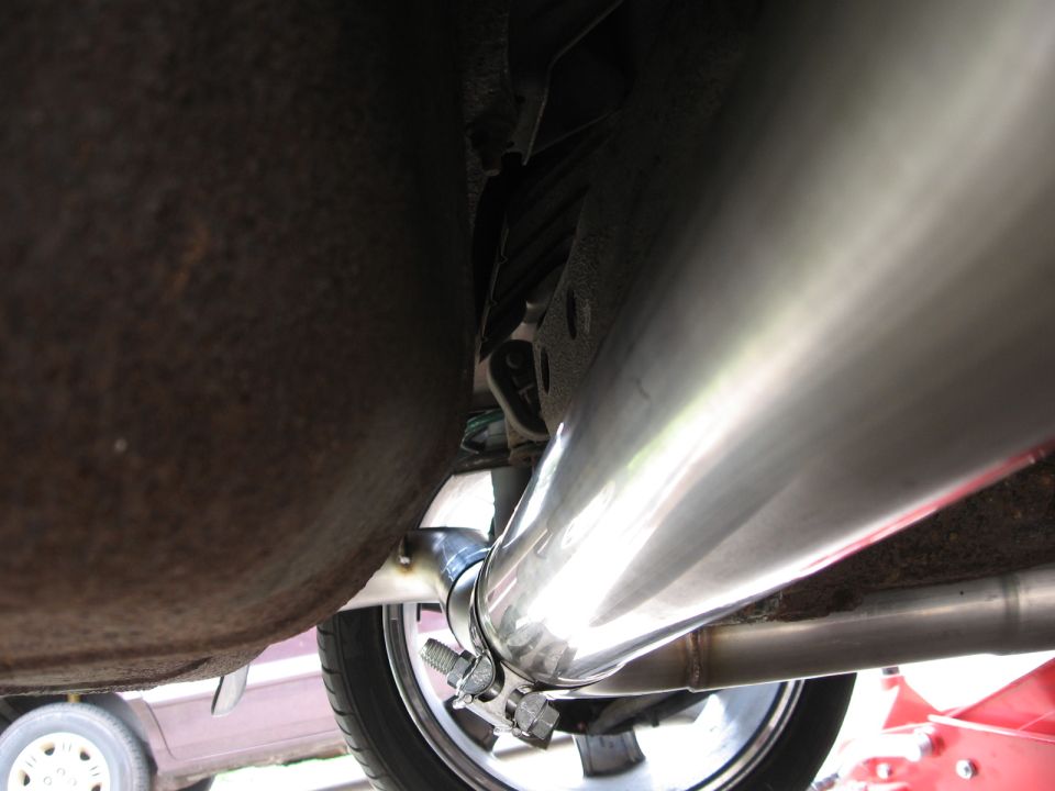 Close-up of a shiny exhaust pipe clamped to the undercarriage of a vehicle, with a rusty section visible
