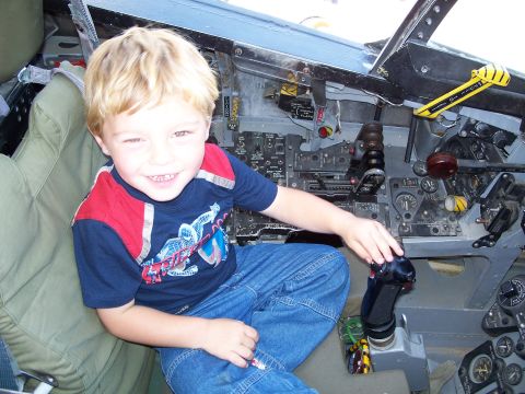 1990 Ford Bronco - A young boy smiles while sitting in the complex cockpit of an aircraft.