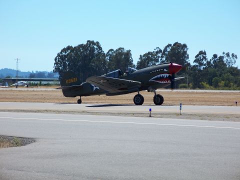 1990 Ford Bronco - A P-40 Warhawk airplane, identified by its shark teeth nose art and tail number 113521, sits on an airport tarmac.
