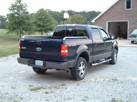 2005 Ford F-150 - A dark blue Ford F-150 pickup truck is parked on a gravel driveway in front of a brick house.