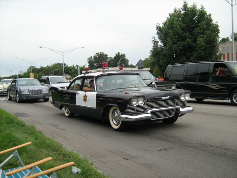 1988 Mercury Grand Marquis - A classic Plymouth police car cruises down the road alongside other vehicles.