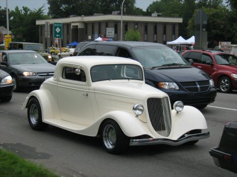 1988 Mercury Grand Marquis - A classic 1934 Ford coupe cruises down the road with other vehicles around it.