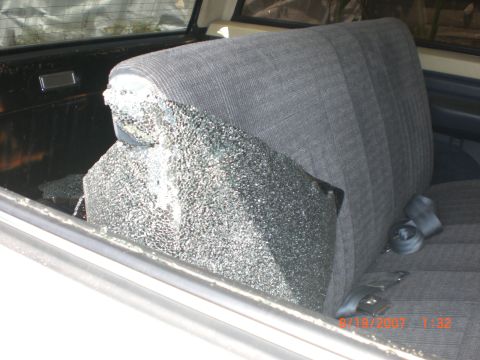1991 Ford Bronco - The rear window of a vehicle is shattered, with glass fragments on the seat and floor.