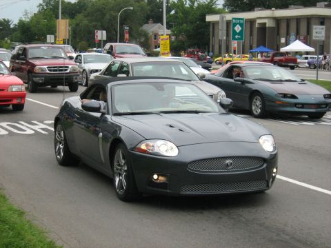 1988 Mercury Grand Marquis - A dark gray Jaguar XK convertible is seen driving in traffic on a street.