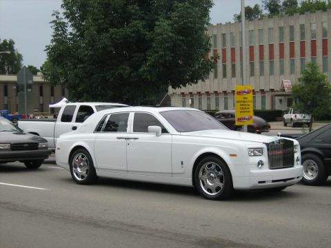 1988 Mercury Grand Marquis - A white Rolls-Royce sedan is seen on the road, with other vehicles and buildings in the background.