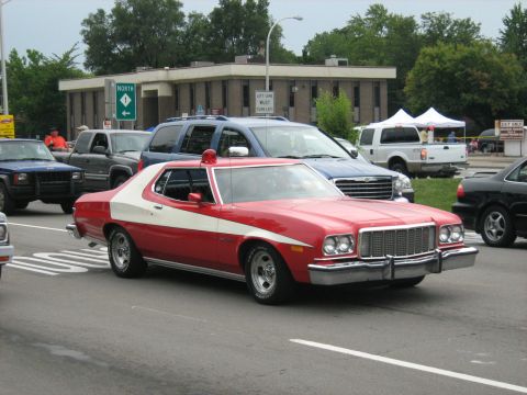 1988 Mercury Grand Marquis - A red and white police car drives down the road, surrounded by other vehicles.