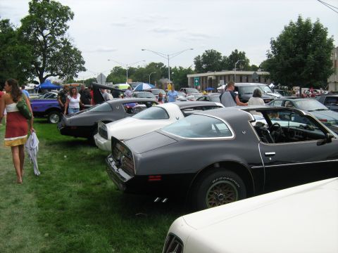 1988 Mercury Grand Marquis - A row of Pontiac Firebirds are displayed at a car show, with a woman walking by in the foreground.