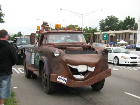 1988 Mercury Grand Marquis - Custom tow truck with Mater face drives down the road, a white Mustang is visible behind it.