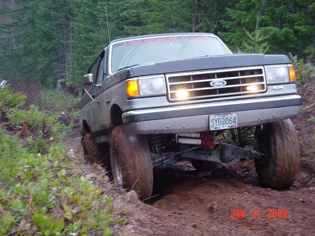 Dark Ford pickup with headlights blazing climbing a red-dirt muddy hill, front view