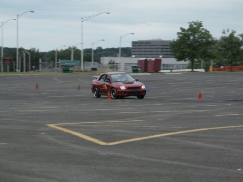 2001 Mercury Grand Marquis - A red Subaru WRX navigates a course marked by orange cones on a cloudy day.