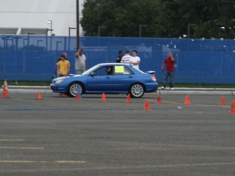 2001 Mercury Grand Marquis - A blue Subaru Impreza WRX sedan navigates a course marked by orange cones, with spectators in the background.
