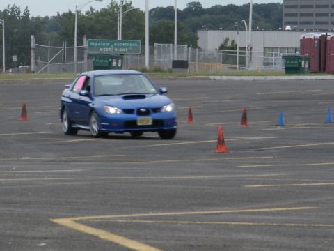 2001 Mercury Grand Marquis - A blue Subaru Impreza WRX navigates an autocross course with orange and blue cones marking the path.