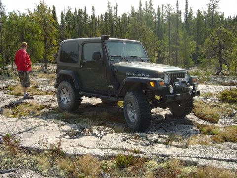 1986 Ford F-150 - A Jeep Wrangler Rubicon is parked on a rocky, wooded landscape, with a person standing nearby.
