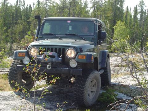 1986 Ford F-150 - A green Jeep Wrangler Rubicon navigates a rocky, wooded trail.