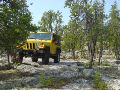1986 Ford F-150 - A yellow Jeep Wrangler navigates a , rocky trail surrounded by trees.