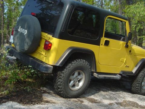 1986 Ford F-150 - A yellow Jeep Wrangler navigates a rocky trail surrounded by trees.