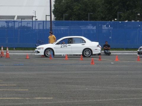 2001 Mercury Grand Marquis - A white sedan is parked on an asphalt lot, surrounded by orange traffic cones, with people standing nearby.