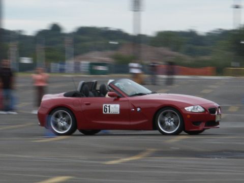 2001 Mercury Grand Marquis - A red convertible sports car is captured in motion on a race track with blurred background figures.