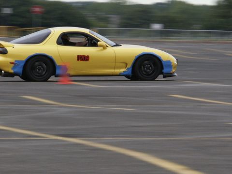 2001 Mercury Grand Marquis - A yellow Mazda RX-7 is seen on a race track with orange cones marking the course.