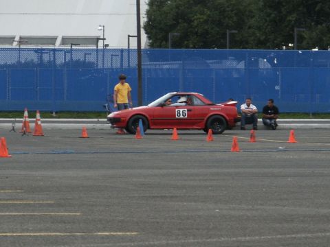 2001 Mercury Grand Marquis - A red sports car is positioned on a paved lot, surrounded by orange traffic cones, with spectators observing.