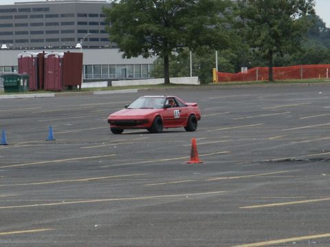 2001 Mercury Grand Marquis - A red sports car navigates a cone course in a large parking lot, with a building and trees in the background.